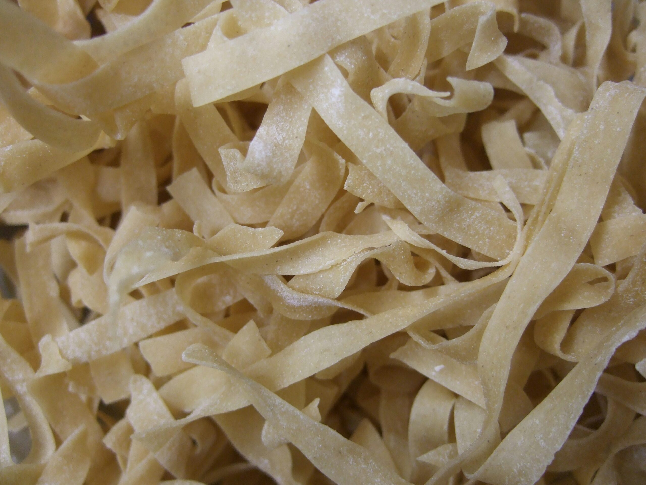 Handgemachte Tagliatelle – breite, goldgelbe Nudeln, leicht mit Mehl bestäubt und bereit für kräftige Saucen.